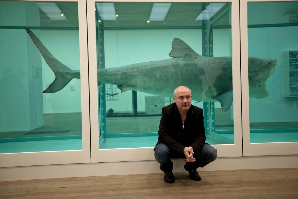 British artist Damien Hirst beside the 1991 piece "The Physical Impossibility of Death in the Mind of Someone Living", a tiger shark preserved in formaldehyde in a vitrine, during a media preview of the first substantial survey show of his work in the UK at the Tate Modern gallery in London, Monday, April 2, 2012.  The exhibition, timed for the culmination of the Cultural Olympiad and due to open to the public on Wednesday, showcases over 70 of Hirst's works since he first came to public attention in 1988.  (AP Photo/Matt Dunham)