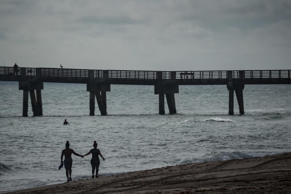 A couple walks the beachfront north of the William O. Lockhart Pier in Lake Worth Beach, Fla. The beachfront was the scene of a suspected sexual assault of a Palm Beach Central student in 2021. Now, five school district employees face felony charges for failing to report the abuse.