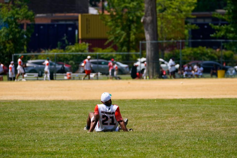 A softball player sits in the outfield in between innings at Votee Park in Teaneck as temperatures rise to 98 degrees on Sunday, July 24, 2022.