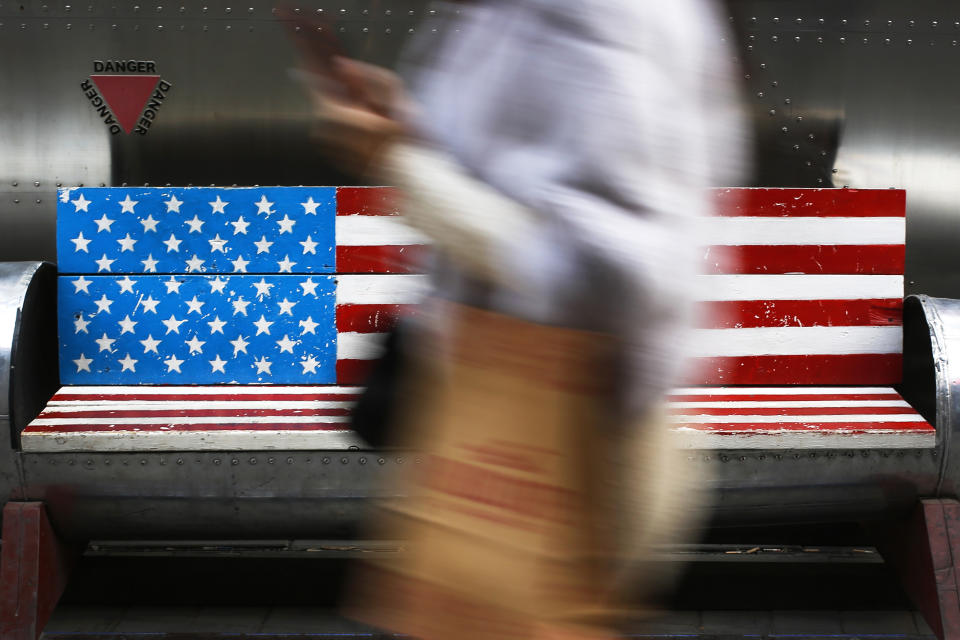 FILE- In this Jan. 6, 2019, file photo, a woman walks by a bench painted with an American flag at the capital city's popular shopping mall in Beijing. Companies making everything from computers to construction cranes are seeing their profits hurt as the United States’ trade war with China causes the world’s second largest economy to slow. (AP Photo/Andy Wong, File)