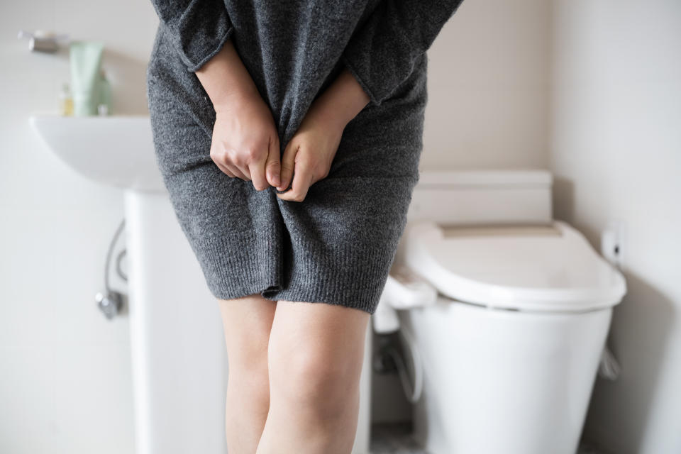 A woman wearing knitwear is complaining of pain from urinary incontinence in front of the toilet