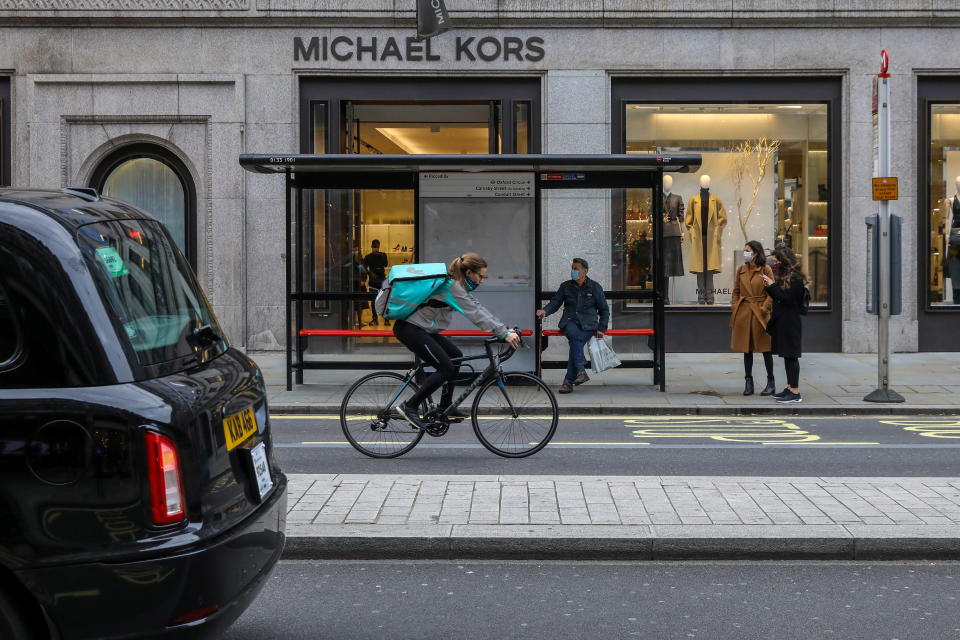 A taxi passes a Deliveroo rider as people wait at a bus stop in Regent Street, one of London's main shopping streets, a day after a new lockdown was announced during the coronavirus disease (COVID-19) outbreak in London, Britain November 1, 2020.     REUTERS/Kevin Coombs