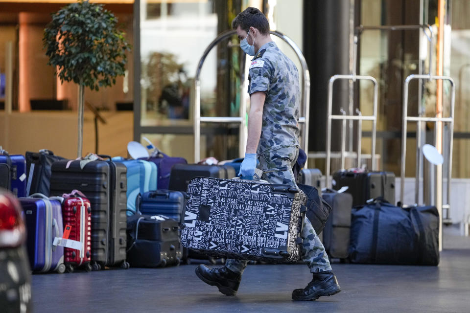 An Australian military person carries luggage for international travelers on their arrival at a quarantine hotel in Sydney, Australia on May 20, 2021. New South Wales state, which includes Sydney, has announced it will end hotel quarantine requirements for fully-vaccinated international travelers from Nov. 1, 2021 in a major relaxation in pandemic restrictions. (AP Photo/Mark Baker)