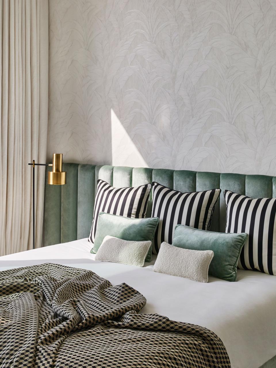 A cheerful guest bedroom with headboard by Humbert & Poyet in Dedar fabric. Bedcover is Osborne & Little;  vintage floor lamp; Arte wallpaper; cushions also in Dedar fabric.