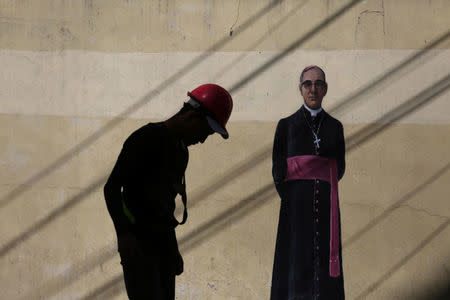 A municipal worker stands by a painting of slain Salvadoran archbishop Oscar Arnulfo Romero in San Salvador, El Salvador, March 7, 2018. REUTERS/Jose Cabezas