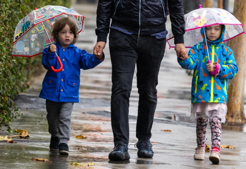 Los Angeles, CA - January 20, 2024: Nerses Sanossian, (CQ) middle, walks her children David, age 3, left, and Amelia, age 5, in the light rain in Pasadena, CA, on Saturday morning January 20, 2024. Nerses says his children love trains. They are walking to the train station to enjoy the Metro ride. (Francine Orr/ Los Angeles Times)