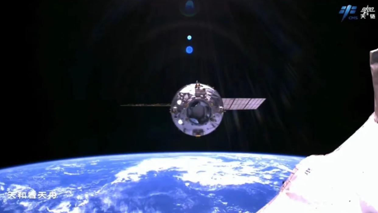  A spacecraft departs a space station with the curve of earth and the blackness of space in the background. 