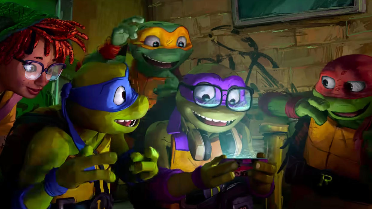  (L to R) April, Leonardo, Michelangelo, Donatello and Raphael in Teenage Mutant Ninja Turtles: Mutant Mayhem, huddled around a phone. 