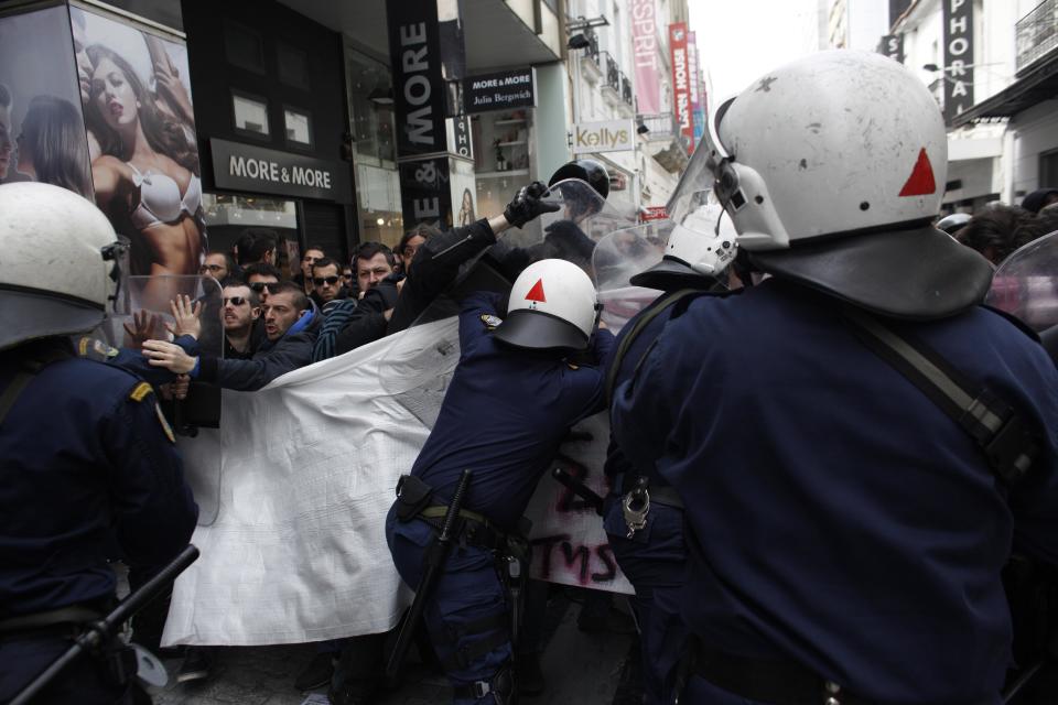 Riot policemen try to disperse demonstrators during a protest against the opening of shops on Sundays and the extension of working hours, in Athens' Ermou shopping street, on Sunday, April 13 2014. Fitch ratings agency warned the successful bond issue didn't mean an end to Greece's financial problems. In a report Friday it said the issue showed the country's progress but doesn't mean it will be able to finance itself on its own when the bailout program ends later this year. (AP Photo/Kostas Tsironis)