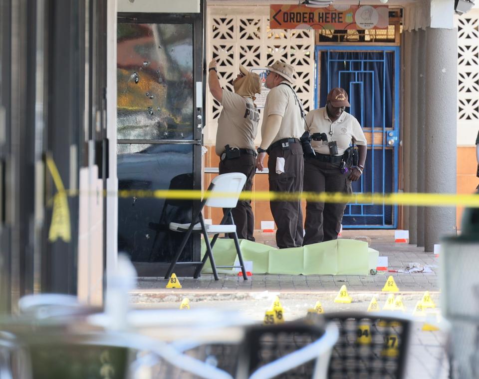 Miami-Dade police investigate near shell case evidence markers on the ground and a door with what appear to be bullet holes (Getty Images)