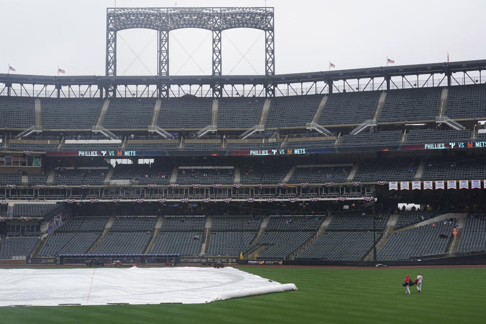 Members of the Philadelphia Phillies staff retrieve some gear during a rain delay before a baseball game between the New York Mets and the Philadelphia Phillies at Citi Field, Thursday, April 15, 2021, in New York. The game was postponed due to rain. (AP Photo/Seth Wenig)