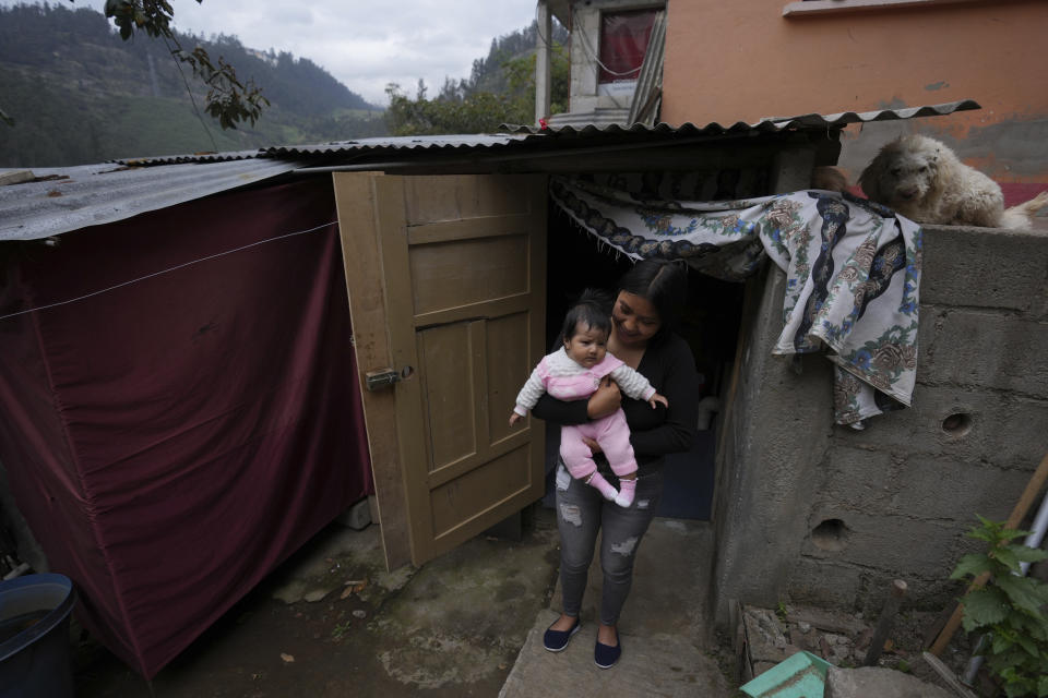 La madre soltera Katherine Gualotuña lleva en brazos a su hija de cuatro meses Arleth fuera de una choza de una habitación donde vive con sus padres en Zámbiza, una población rural al noreste de Quito, Ecuador, el lunes 15 de noviembre de 2022. Gualotuña, que depende de una ayuda económica mensual del gobierno para comprar comida para su bebé considerado vulnerable ante desnutrición, trabaja en su tesis para graduarse como tecnóloga en mecánica industrial. Dijo que su mayor deseo es tener “dinero para marcharse de ahí y construir una casita”. (AP Foto/Dolores Ochoa)