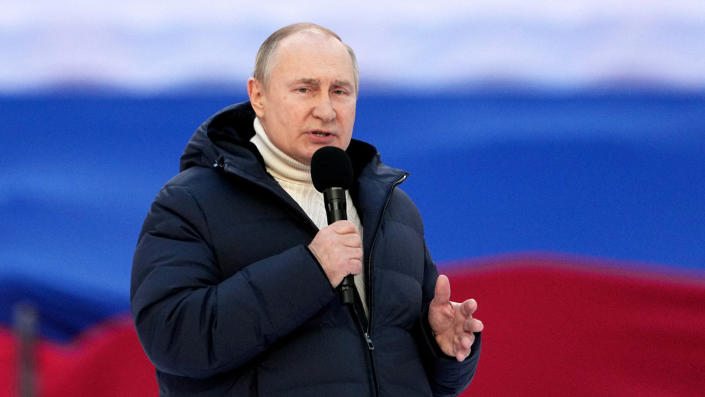 Russian President Vladimir Putin, in a winter jacket and polo neck sweater, talks into a microphone.