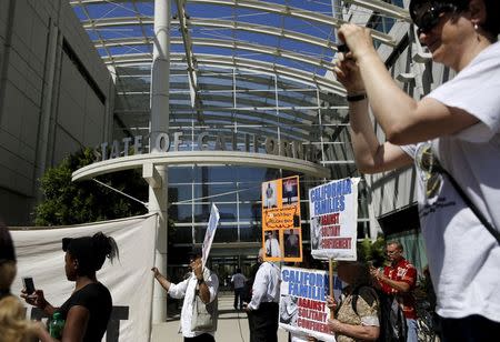 People carry signs at a rally outside the Elihu Harris state building in Oakland, California, September 1, 2015. REUTERS/Robert Galbraith