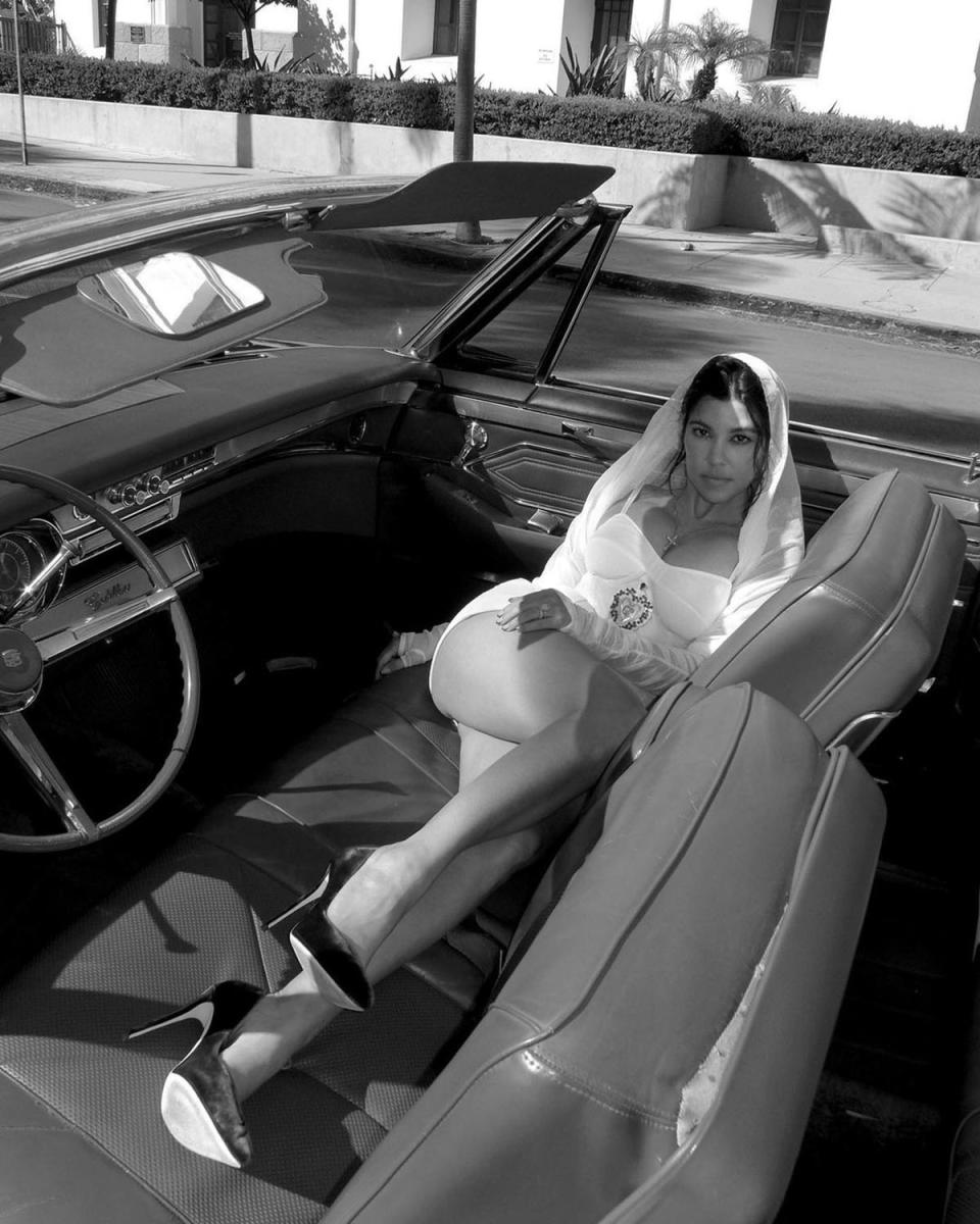 Kourtney Kardashian poses in a white dress and white veil, in a vintage car.