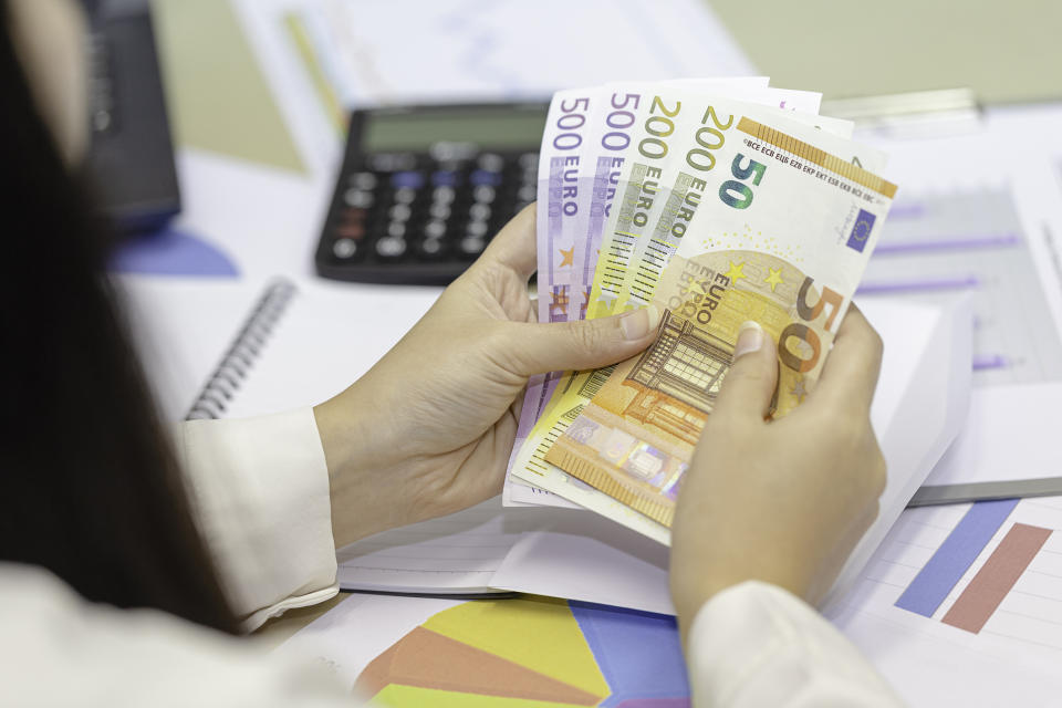 Person counting Euro banknotes over financial charts
