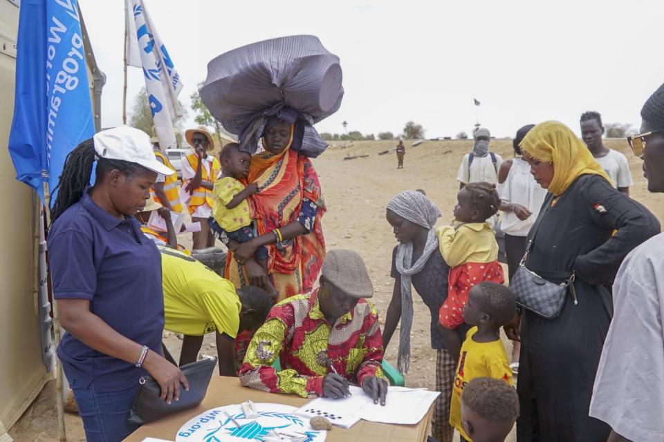 Women and children line up to check in at a table.