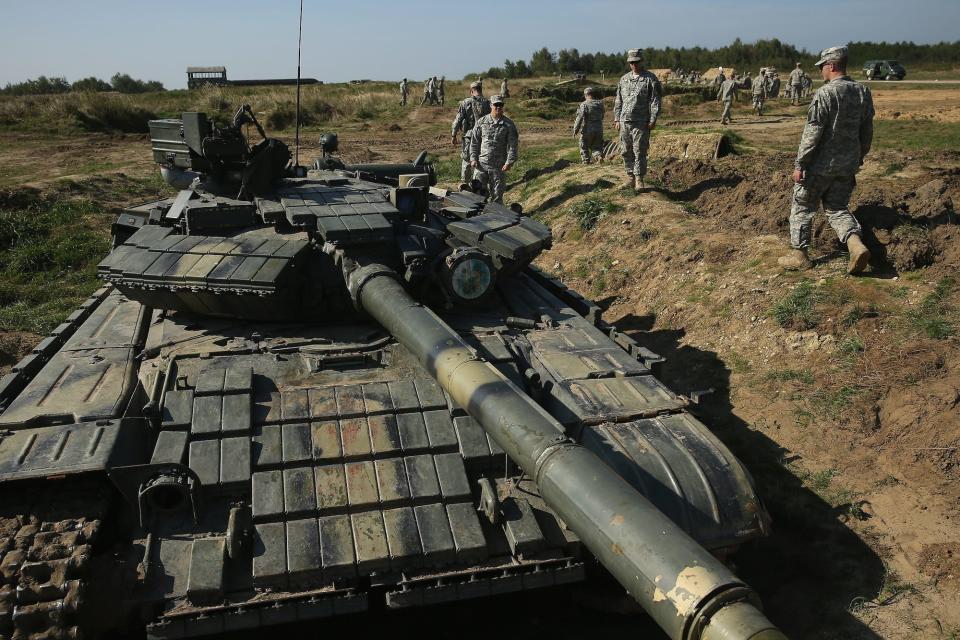 Soldiers standing next to a tank.