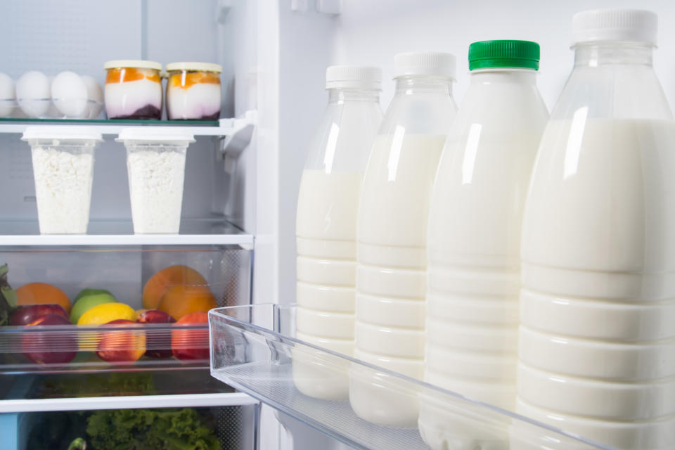 a close-up of bottled milk, lying on a shelf in the refrigerator door, against the background of products, fruits, vegetables, cottage cheese, eggs and yogurt