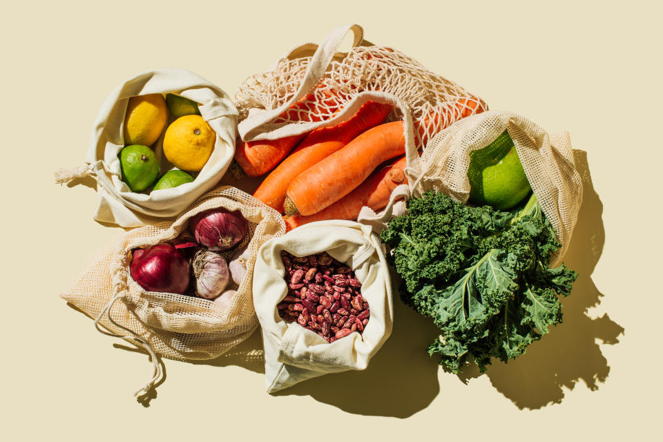 Variety Fresh of organic fruits and vegetables and healthy vegan meal ingredients in reusable eco cotton bags on beige background . Zero waste shopping concept. Healthy food, clean eating, eco friendly, no plastic. Flat lay, top view