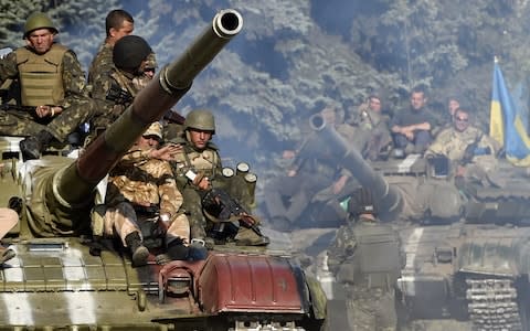 Ukrainian army soldiers ride a tank on a road near where pro-Russian separatists fired heavy artillery