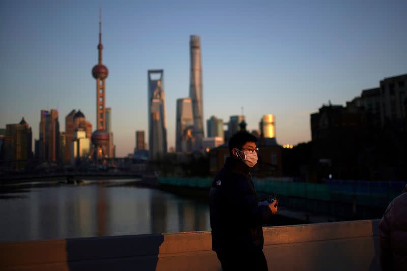 A man wearing a face mask walks on a bridge in front of the financial district of Pudong in Shanghai