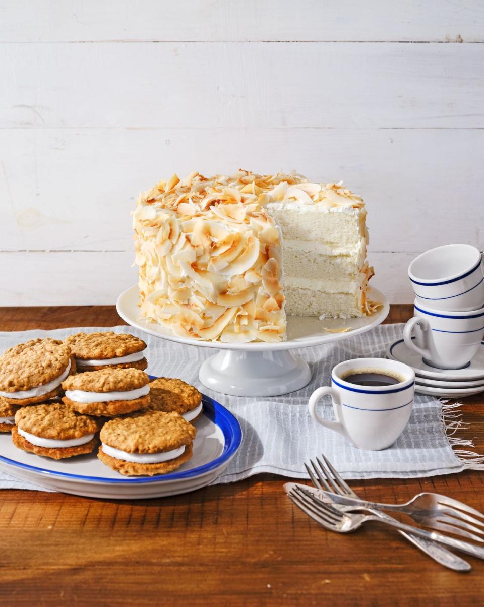 coconut angel cake covered in toasted coconut on a white cake stand with a cup of coffee to the side