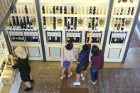 A group of people look to select wines from a dispensary at the Oakville Wine Merchant Friday, June 12, 2020, in Oakville, Calif. California wineries started uncorking their bottles and welcoming people back to their tasting rooms Friday as the state's $145 billion tourism industry gears up with hotels, zoos, museums and aquariums also allowed to reopen. The wine retail experience in Oakville features 50 different wines by the taste or glass and is open to the public without an appointment. (AP Photo/Eric Risberg)