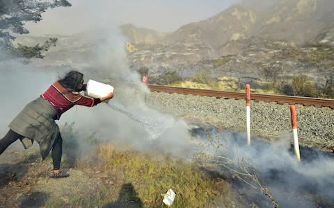 Songsri Kesonchampa tosses a bucket of water on to burning embers across the road from her home  - Credit: AFP