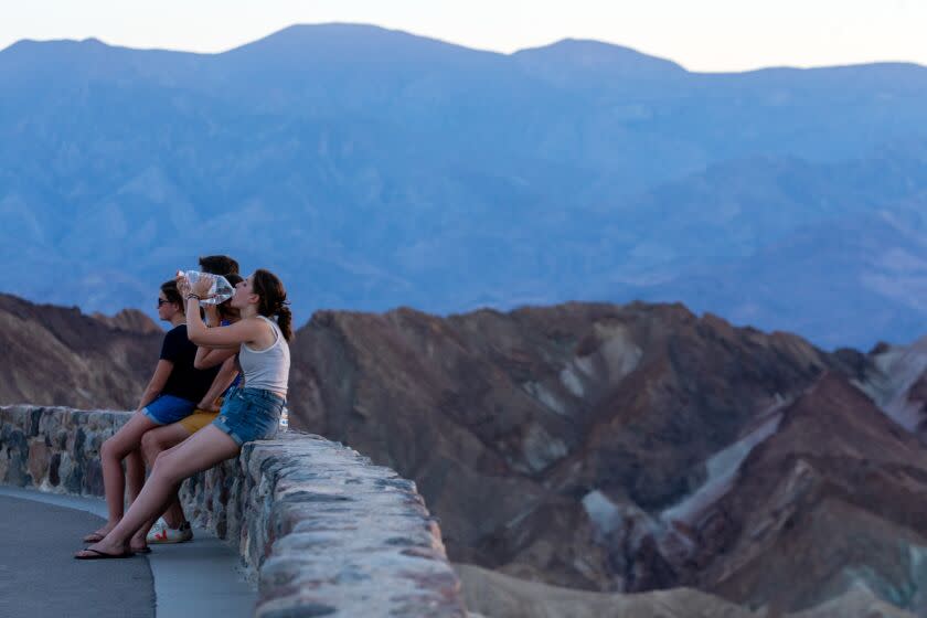 Death Valley, CA - July 16: Marie David, 16, of France, middle, drinks water to keep hydrated at Zabriskie Point on Sunday, July 16, 2023, in Death Valley, CA. With the wind, it feels a bit cooler at 123 degrees this evening in Death Valley, CA. (Francine Orr / Los Angeles Times)