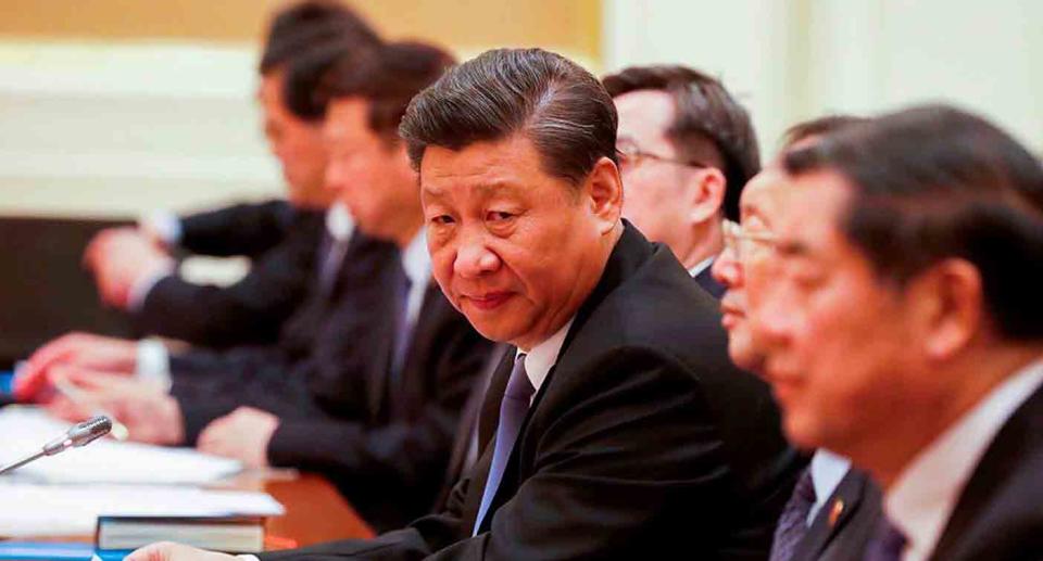 Xi Jinping sits at a desk with CCP members and looks left at the camera.