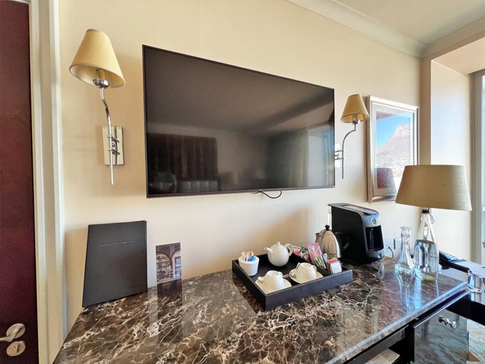 Hotel room with flat-screen TV, sconces on either side, and a marble tabletop with a tea set and coffee maker in front