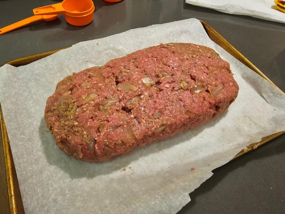 Ground beef formed into a loaf shape on a piece of parchment paper on a cookie sheet