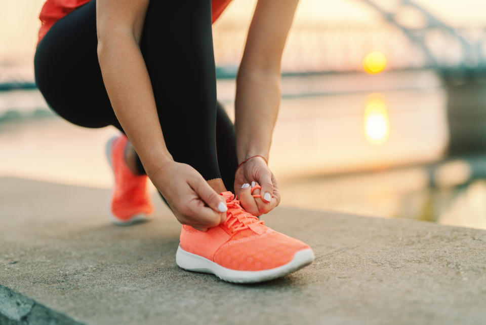 Close up of sporty woman tying shoelace while kneeling outdoor, In background bridge. Fitness outdoors concept.