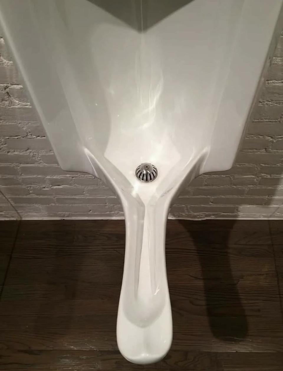 Urinal with an unusual, sleek design against a textured wall