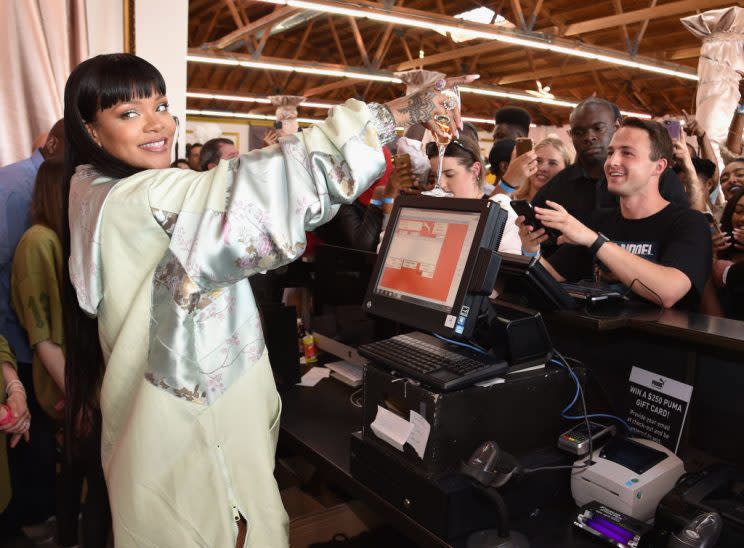 Rihanna, accessorized with a wine glass, worked behind the counter at the Fenty x Puma pop-up shop in L.A. on Tuesday. (Photo: Kevin Mazur/Getty Images for PUMA)