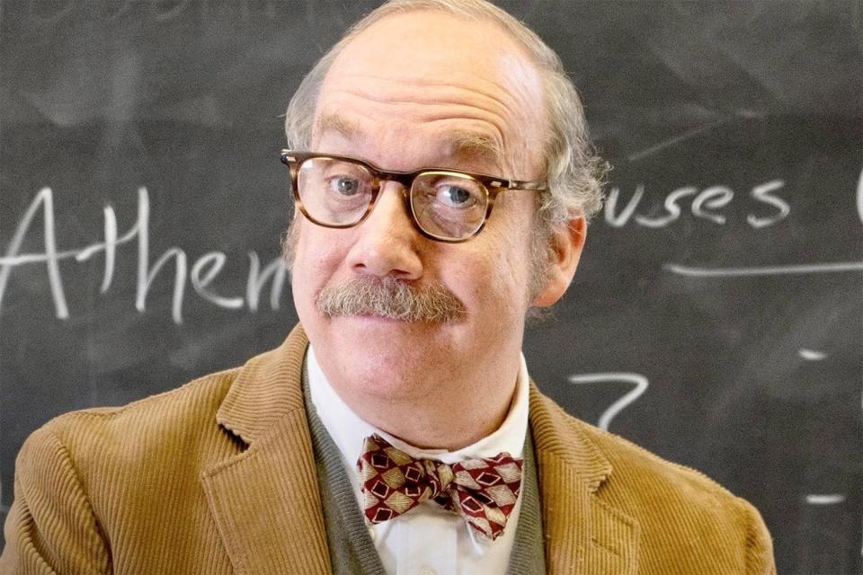 Paul Giamatti looks smugly at the camera and is in front of a chalkboard. 