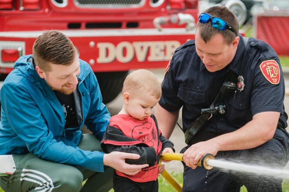 Asher Maarschelk, 18 months, his father, Tyler, left, and firefighter Bo McCaslin, participate in a simulated flame knock-down game with a hose line during the celebration of the Dover Fire Department's 150th year of operation, Sunday, May 21 at the north station.