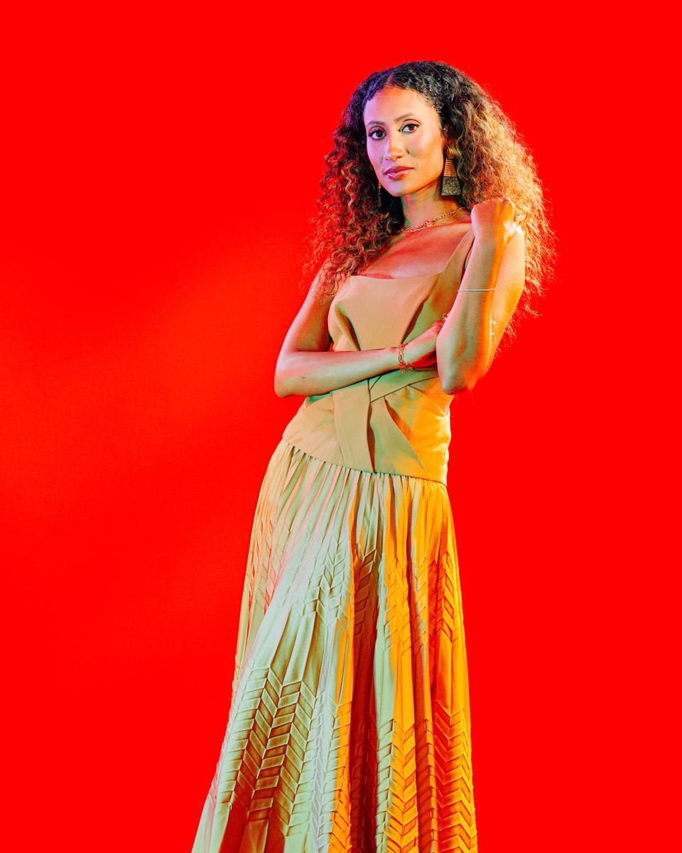 Elaine Welteroth wears an orange top and pleated skirt against a bright red background