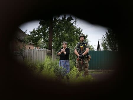 A member of the Ukrainian police special task force "Kiev-1" stands beside a local woman as sappers check her building in the eastern Ukrainian village of Semenovka, near Sloviansk, July 14, 2014. REUTERS/Gleb Garanich