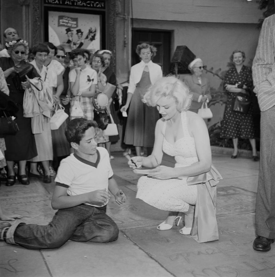 <p>Marilyn had fans of all ages. Here, she signs for a young boy at the Grauman's event. </p>