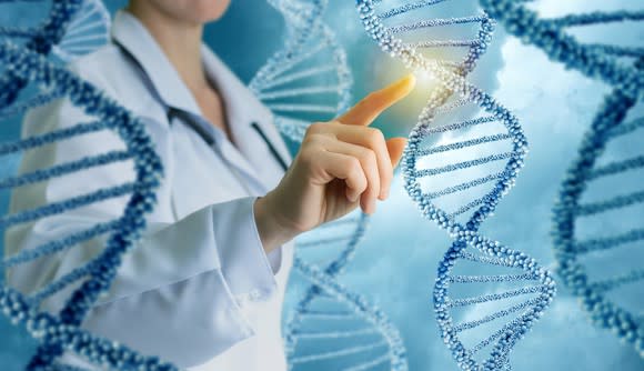 A person in a lab coat points to a double helix among a row of double helixes.