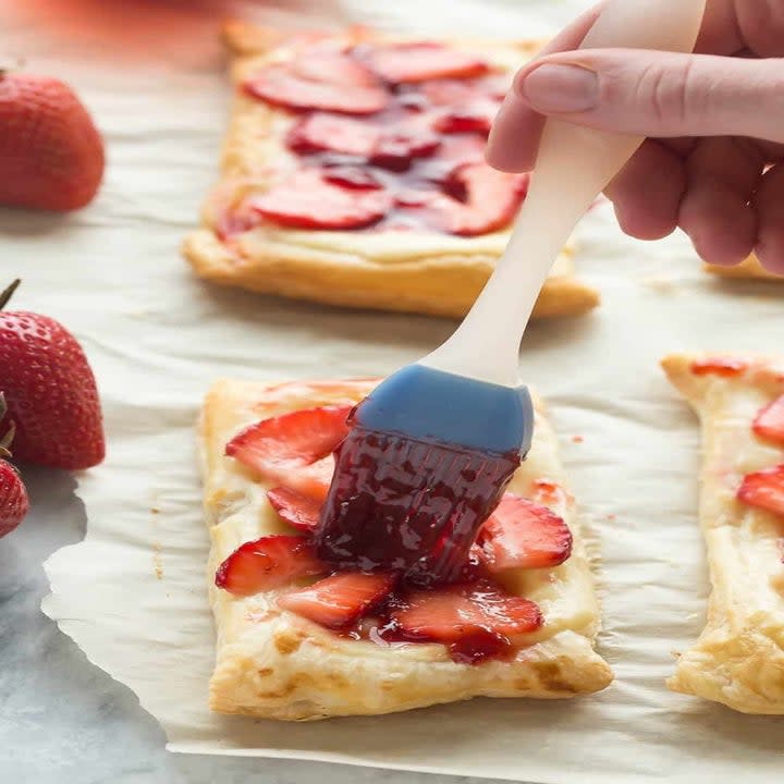 Brushing strawberry cream cheese pastries with jam.