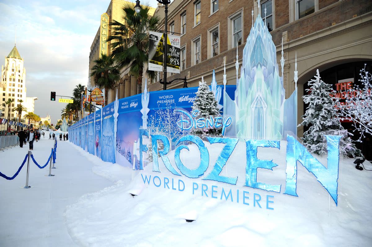 Outside sits a sign that says "Disney Frozen World Premiere" in icy blue. It rests on a bank of fake snow. Fake snow also sits on the sidewalk near it, where you can see people walking. 