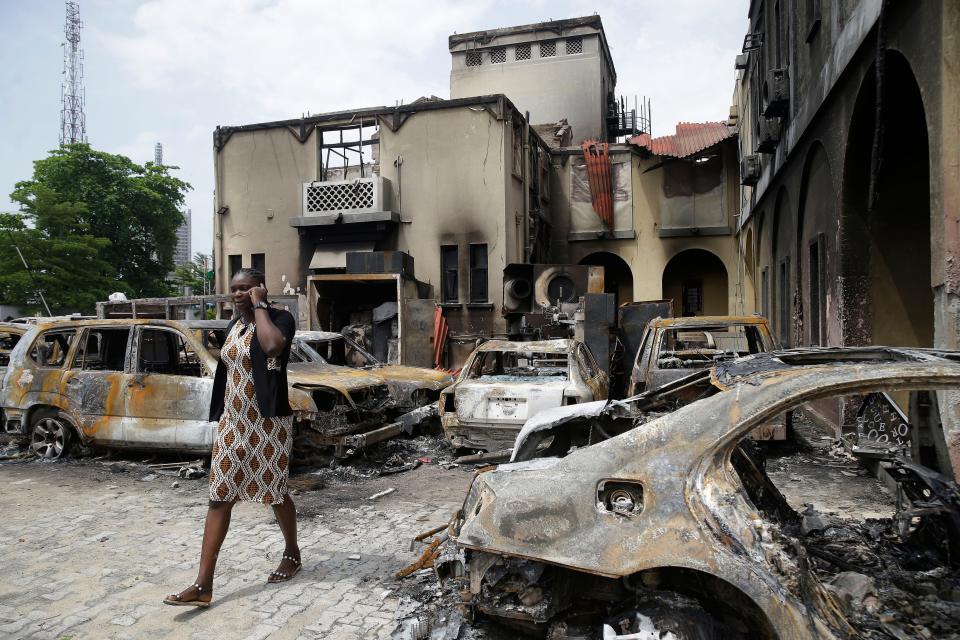 A woman walks past burned cars and a federal high court building in Lagos, Nigeria, Oct. 26, 2020. Nigeria’s top police official on Saturday ordered the immediate mobilization of all officers to “reclaim the public space from criminal elements masquerading as protesters” after days of peaceful demonstrations over police abuses.