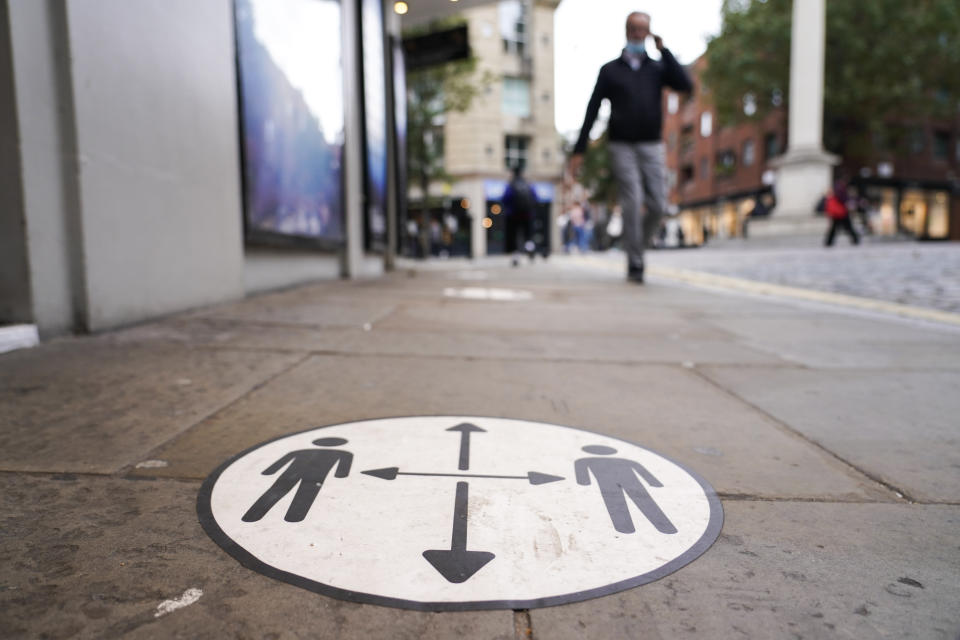 A man walks past a social distancing sign in the area of Covent Garden, in London, Tuesday, Oct. 19, 2021. Many scientists are pressing the British government to re-impose social restrictions and speed up booster vaccinations as coronavirus infection rates, already Europe's highest, rise once more. The U.K. recorded 49,156 new COVID-19 cases on Monday, Oct. 18, the largest number since mid-July. New infections averaged 43,000 a day over the past week, a 15% increase on the week before.(AP Photo/Alberto Pezzali)