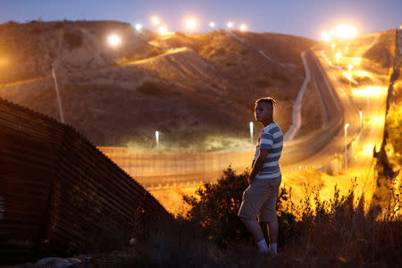 Jimmy Omar Martinez, 22, a migrant from El Salvador, part of a caravan of thousands traveling from Central America en route to the United States, poses in front of the border wall between the U.S. and Mexico in Tijuana, Mexico, November 23, 2018. Martinez said U.S. music videos and Hollywood films have formed his vision of the American Dream. "I want to go to Miami because it looks so nice in films like 'Fast and Furious'," he said. "I want to be there to have more security and a better future." REUTERS/Kim Kyung-Hoon SEARCH "KYUNG-HOON DREAMS" FOR THIS STORY. SEARCH "WIDER IMAGE" FOR ALL STORIES.