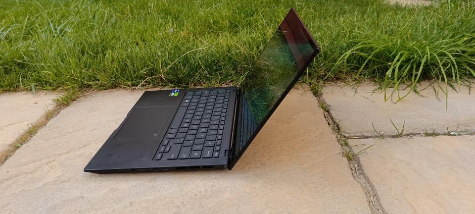 A black ASUS Zenbook Pro 14 OLED sitting on a patio in front of a grassy lawn