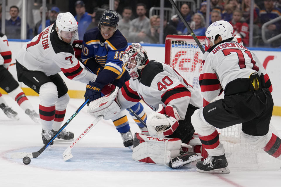 St. Louis Blues' Brayden Schenn (10) reaches for a loose puck along with New Jersey Devils goaltender Akira Schmid (40), Dougie Hamilton (7) and Jonas Siegenthaler (71) during the second period of an NHL hockey game Friday, Nov. 3, 2023, in St. Louis. (AP Photo/Jeff Roberson)