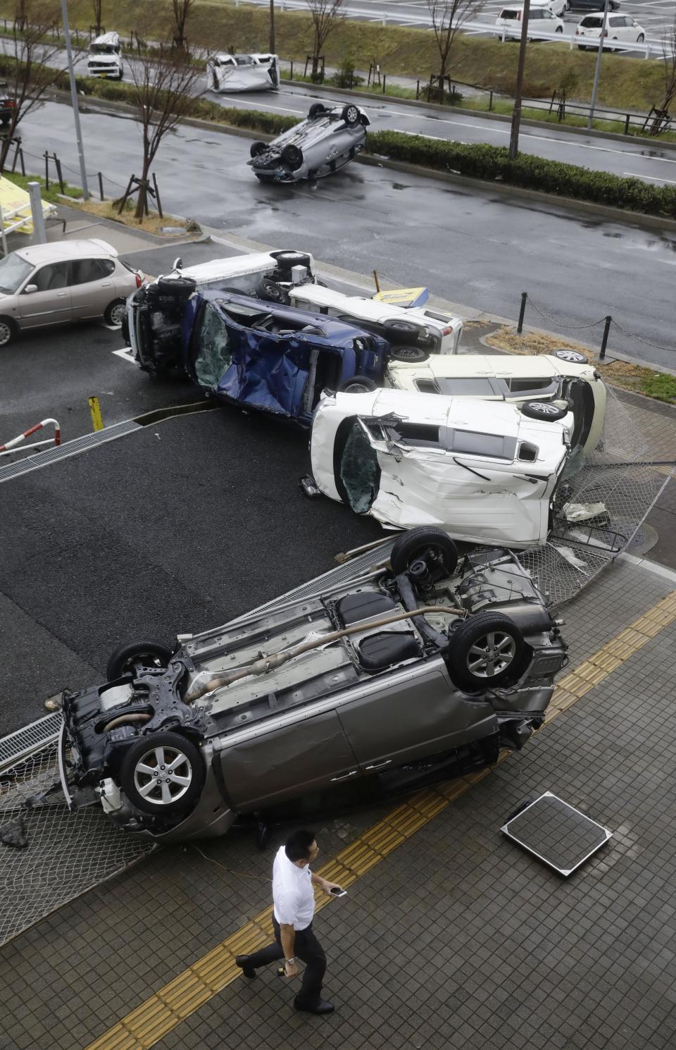 Overturned cars are seen on street following a powerful typhoon in Osaka, western Japan, Tuesday, Sept. 4, 2018. A powerful typhoon blew through western Japan on Tuesday, causing heavy rain to flood the region's main offshore international airport and high winds to blow a tanker into a connecting bridge, disrupting land and air travel. (Kota Endo/Kyodo News via AP)